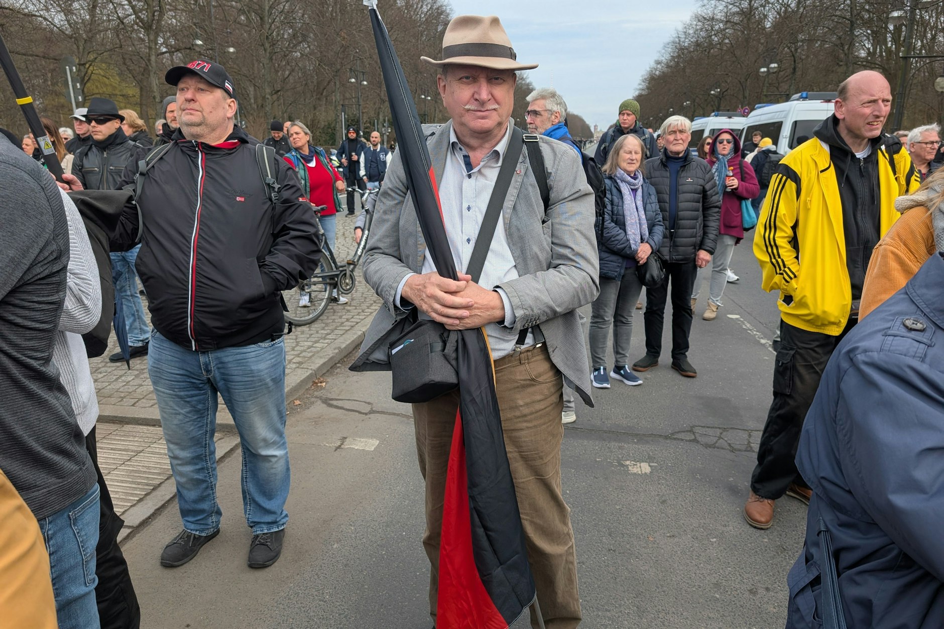 Bernd Pachal steht mit Hut und einer zusammengerollten Deutschlandfahne inmitten der Menschenmenge.