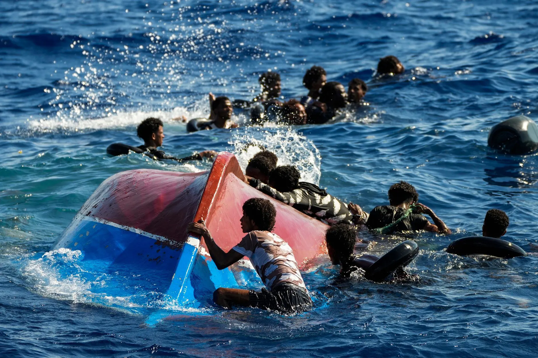 Migranten schwimmen neben ihrem umgestürzten Holzboot im Mittelmeer (Archivbild).