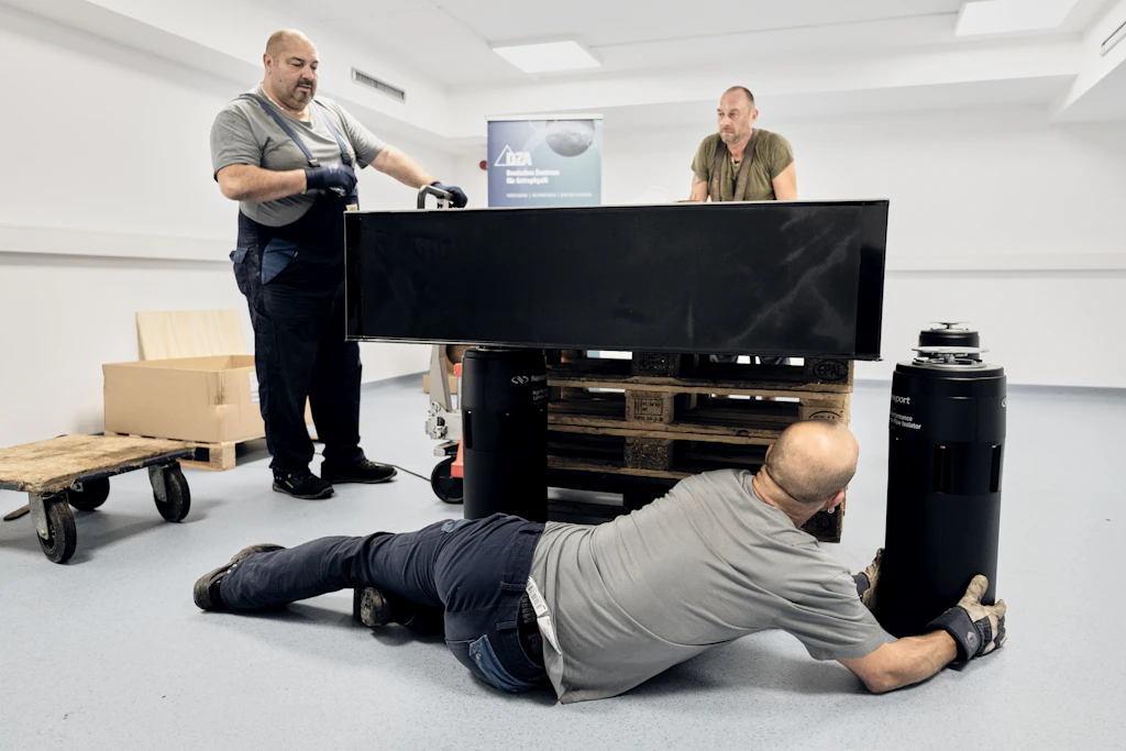 Mitarbeiter einer Transportfirma positionieren einen schwingungsgedämpften Optiktisch in einem Laborgebäude des Deutschen Zentrums für Astrophysik (DZA).