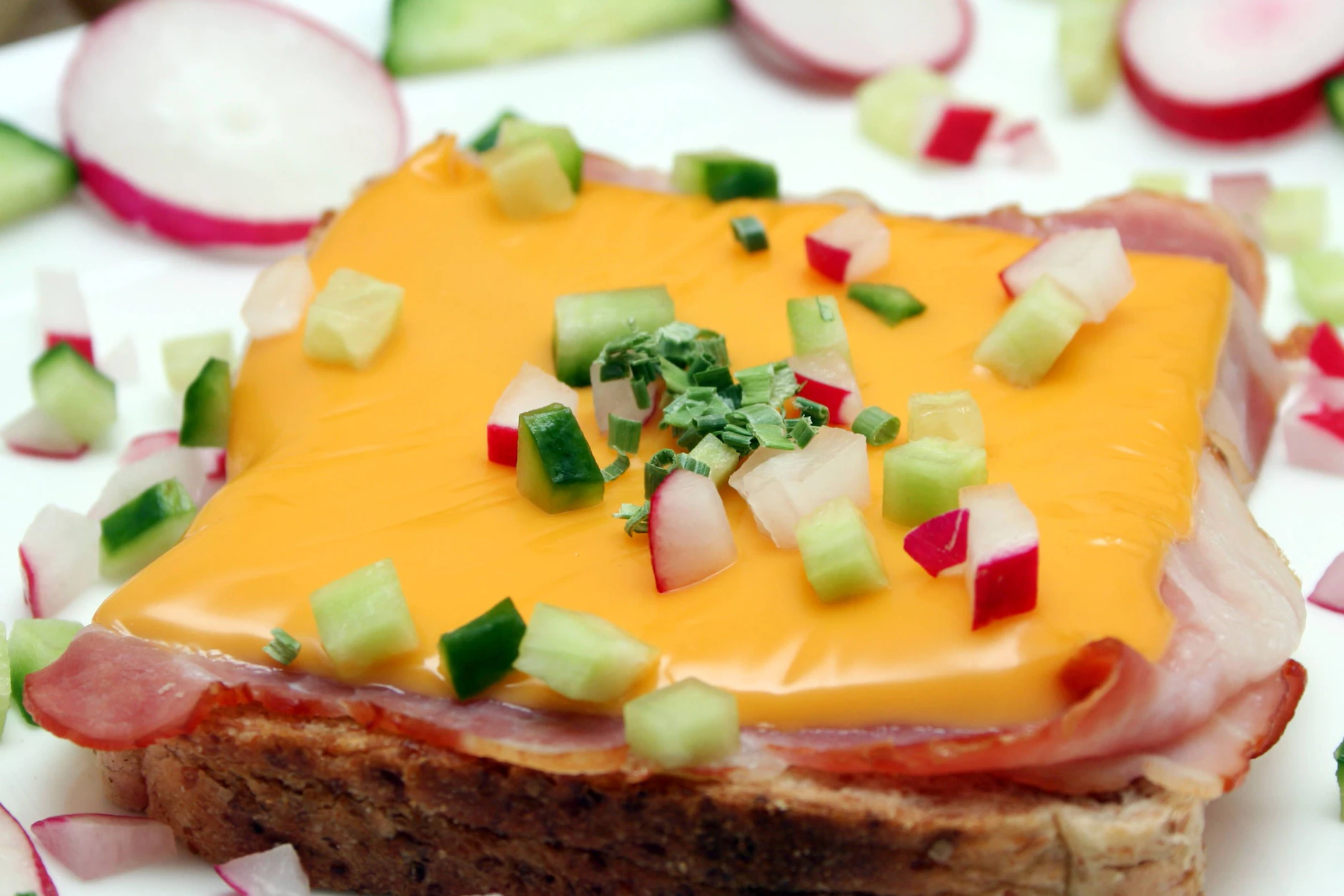 Der Schinken-Toast wird mit Schnittkäse oder Scheiblettenkäse überbacken. Wer will, kann ihn auch mit Gurken- und Radieschen-Stücken garnieren.