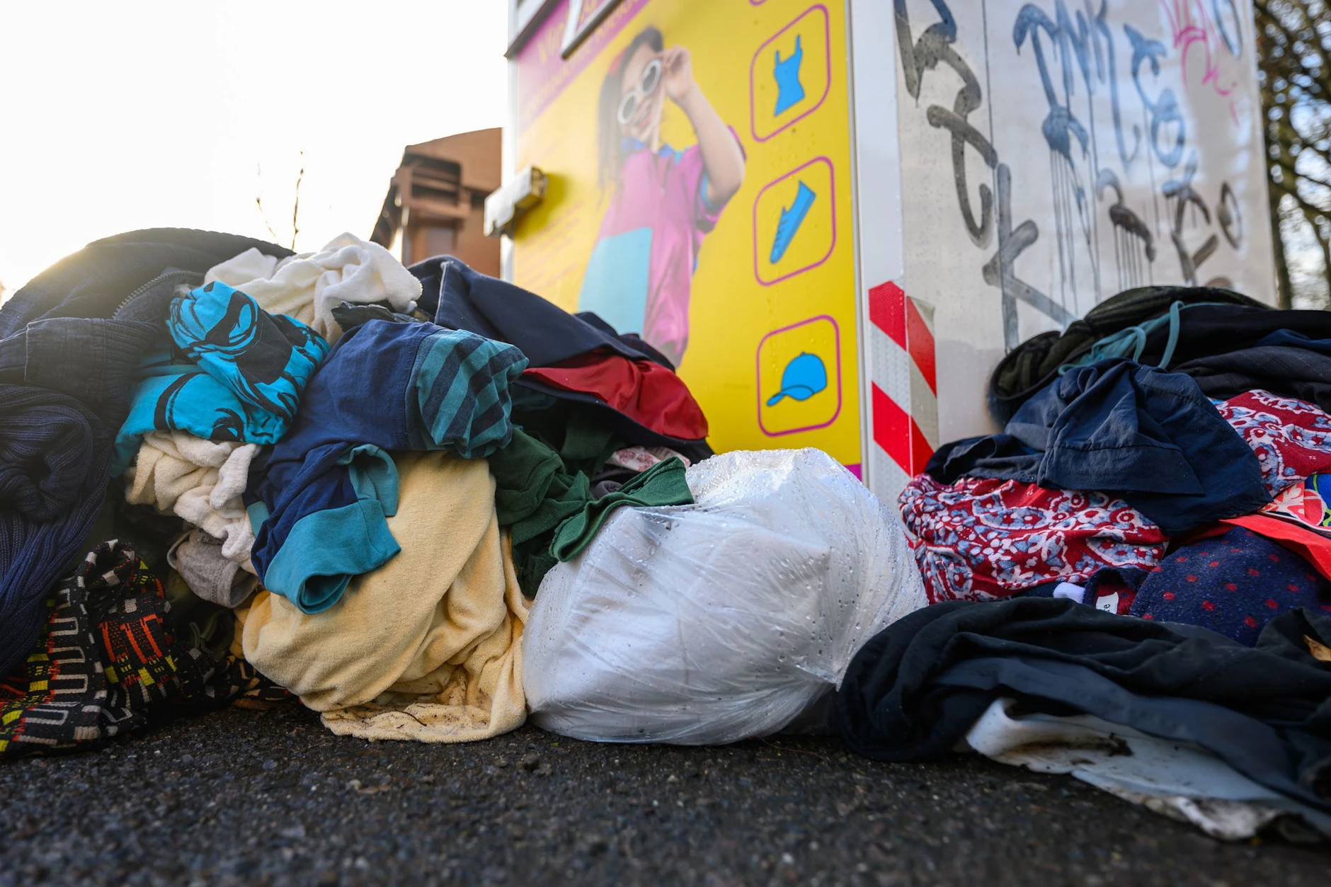 Gebrauchte Kleidungsstücke liegen vor einem Sammelcontainer.