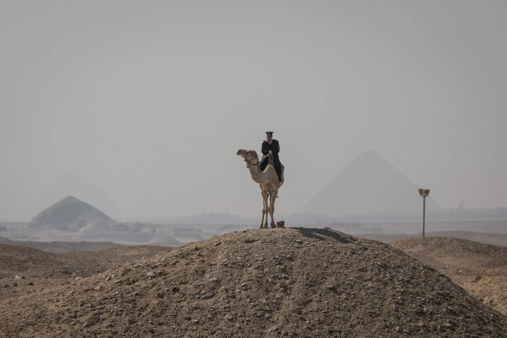 Ein ägyptischer Polizist auf einem Kamel steht Wache in der Nähe der Djoser-Pyramide in Saqqara außerhalb von Kairo, die für viele Touristen ein Muss ist.