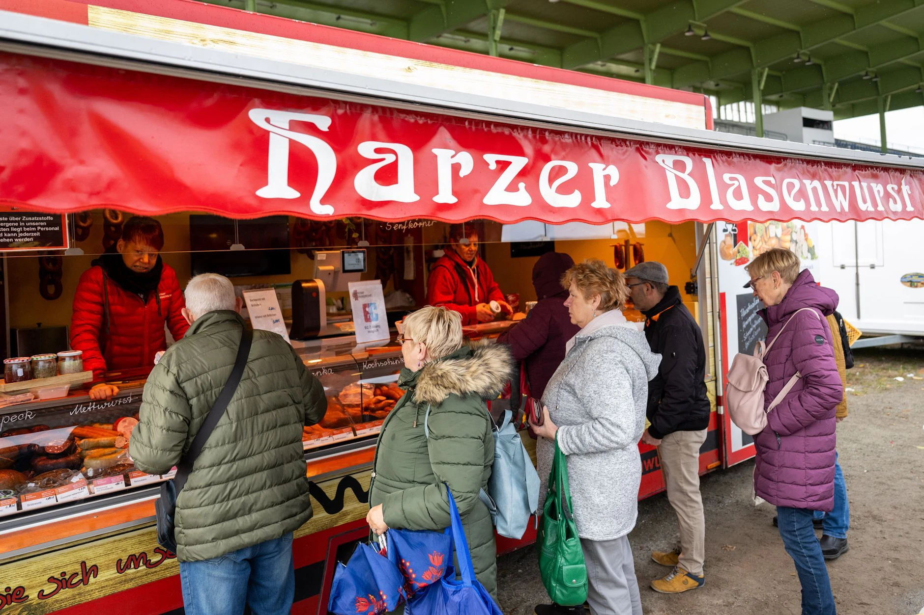 Besucher der „Verkaufsmesse Ostpro“ auf der Trabrennbahn Karlshorst stehen an einem Stand mit Harzer Blasenwurst.