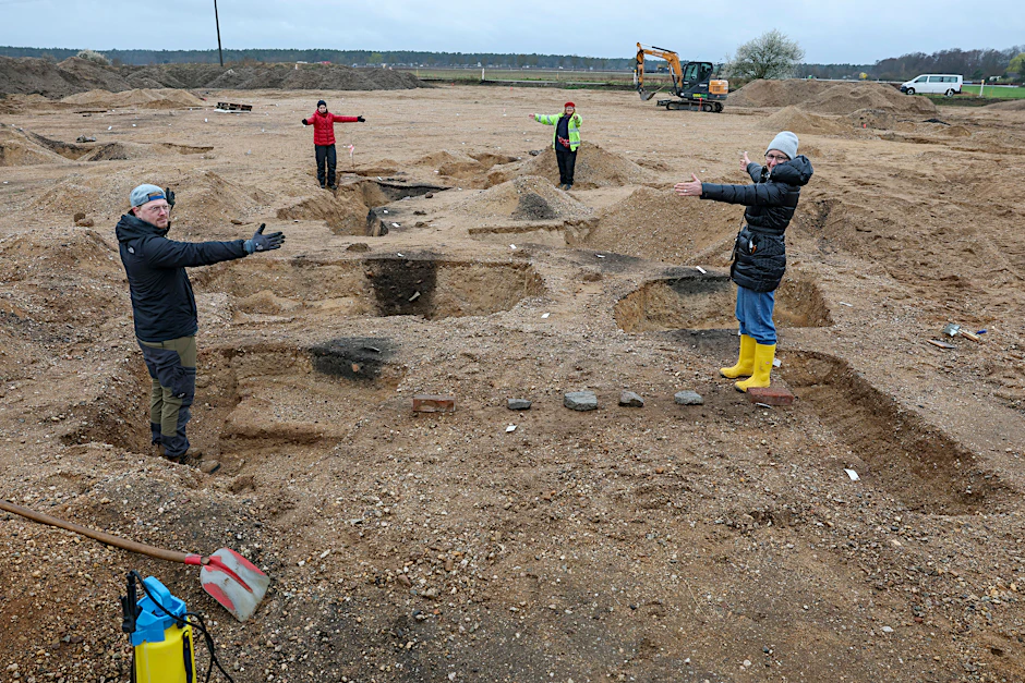 Grabungsteilnehmer und Archäologen demonstrieren die Größe der gefundenen Häuser auf der Grabungsstätte vor dem Bau der Ortsumfahrung von Wellaune (Kreis Nordsachsen).