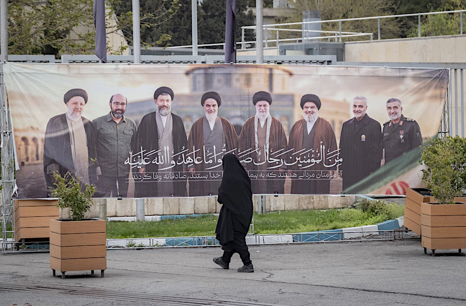 Eine Frau geht in Teheran an einem Banner mit verstorbenen Führungsfiguren vorbei, darunter Ali Chamenei, Ruhollah Chomeini, Hassan Nasrallah und Qassem Soleimani.