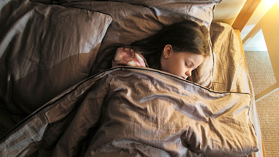 Ein Mädchen schläft von Geräuschen abgeschirmt: Viele Kinder mit ME/CFS können ihr Bett kaum verlassen.