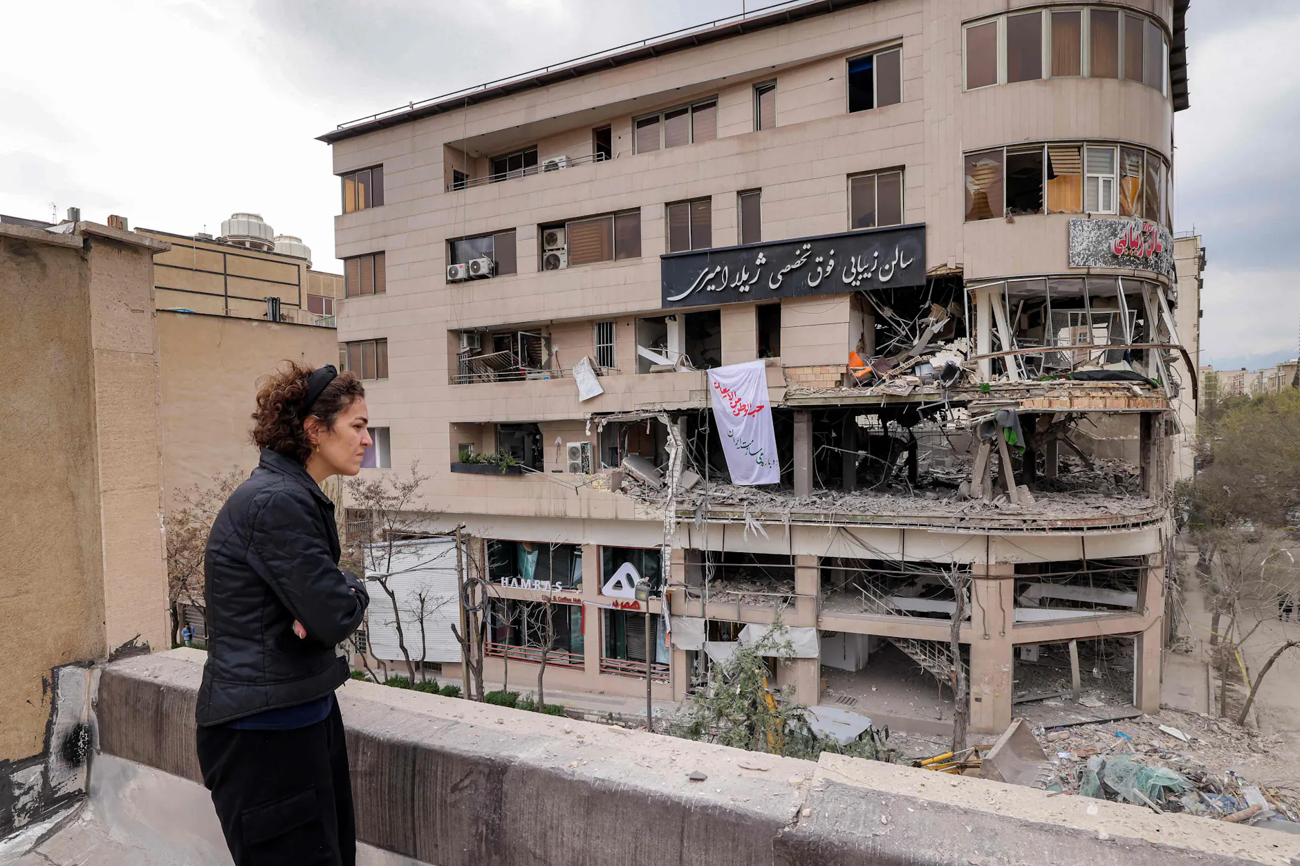 Frau blickt vom Dach auf zerstörtes Al-Araby-TV-Gebäude nach Raketenangriff, Teheran.