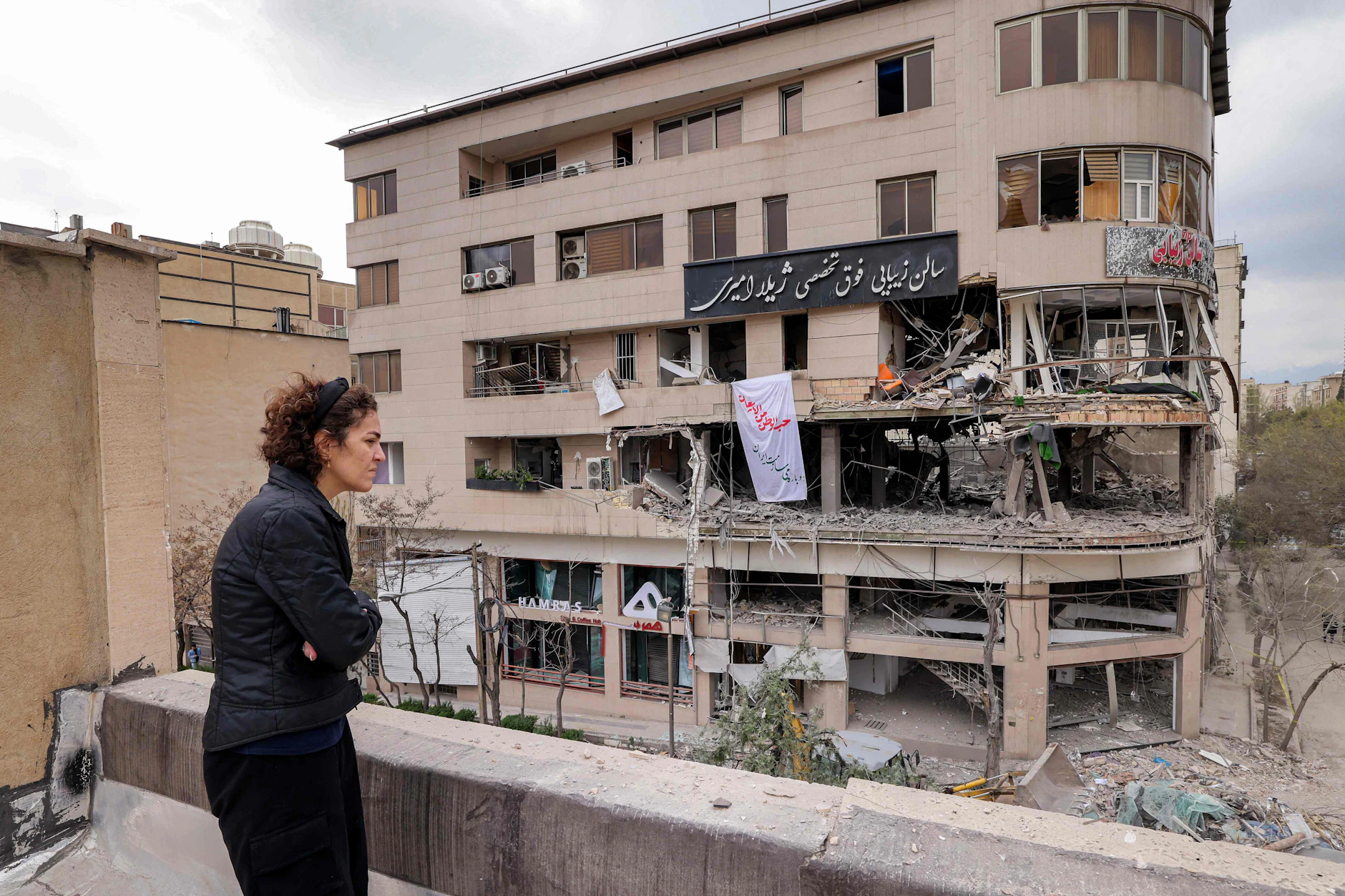 Frau blickt vom Dach auf zerstörtes Al-Araby-TV-Gebäude nach Raketenangriff, Teheran.