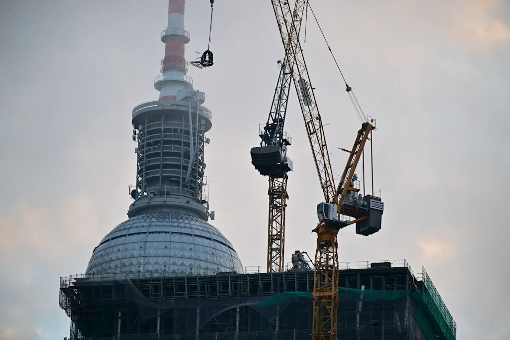 Der Fernsehturm verschwindet hinter dem&nbsp; Büroturm „The Berlinian“ an der Karl-Liebkecht-Straße. Am 14. Januar 2026 schwebte der Richtkranz an einem Kran.