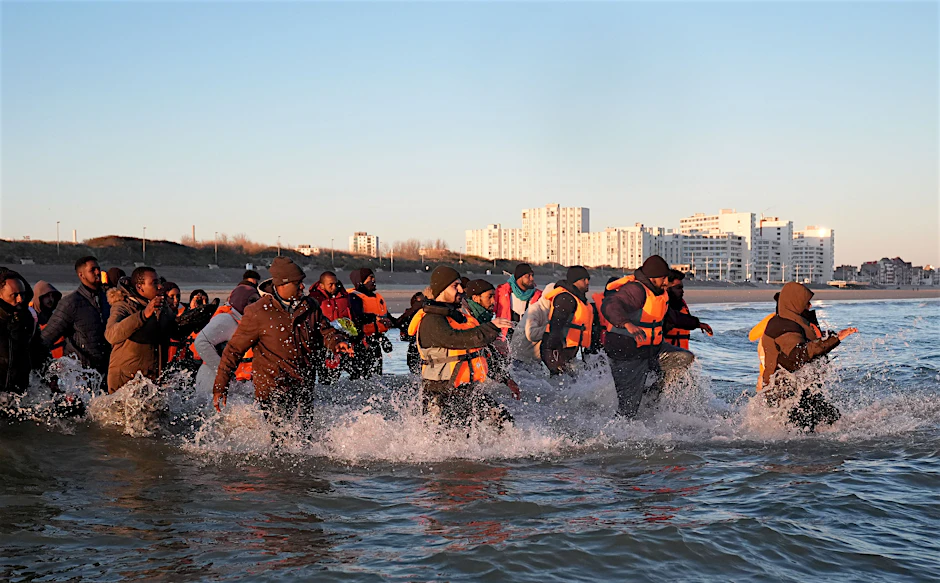 Menschen laufen ins Meer, um an Bord eines kleinen Bootes vor der Küste von Frankreich zu gelangen.