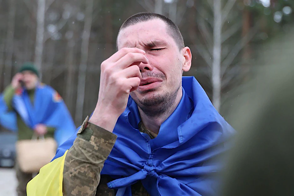 Ein freigelassener ukrainischer Kriegsgefangener bekreuzigt sich nach dem Austausch – in eine Flagge gehüllt.