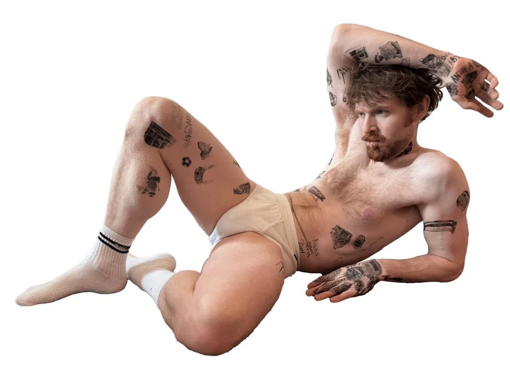 Tätowiertes Modell mit Doppelrippschlüpfer und Tennissocken. Wandbild aus Marc Brandenburgs Werkserie „Tattoos“, 2026, Fotografie