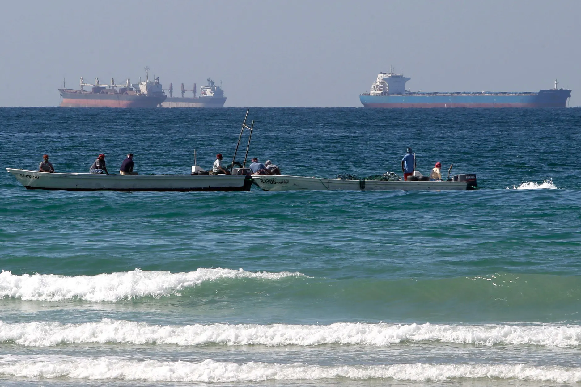 Fischer beobachten von ihren Booten aus, wie sich Frachtschiffe südlich der Straße von Hormus stauen.