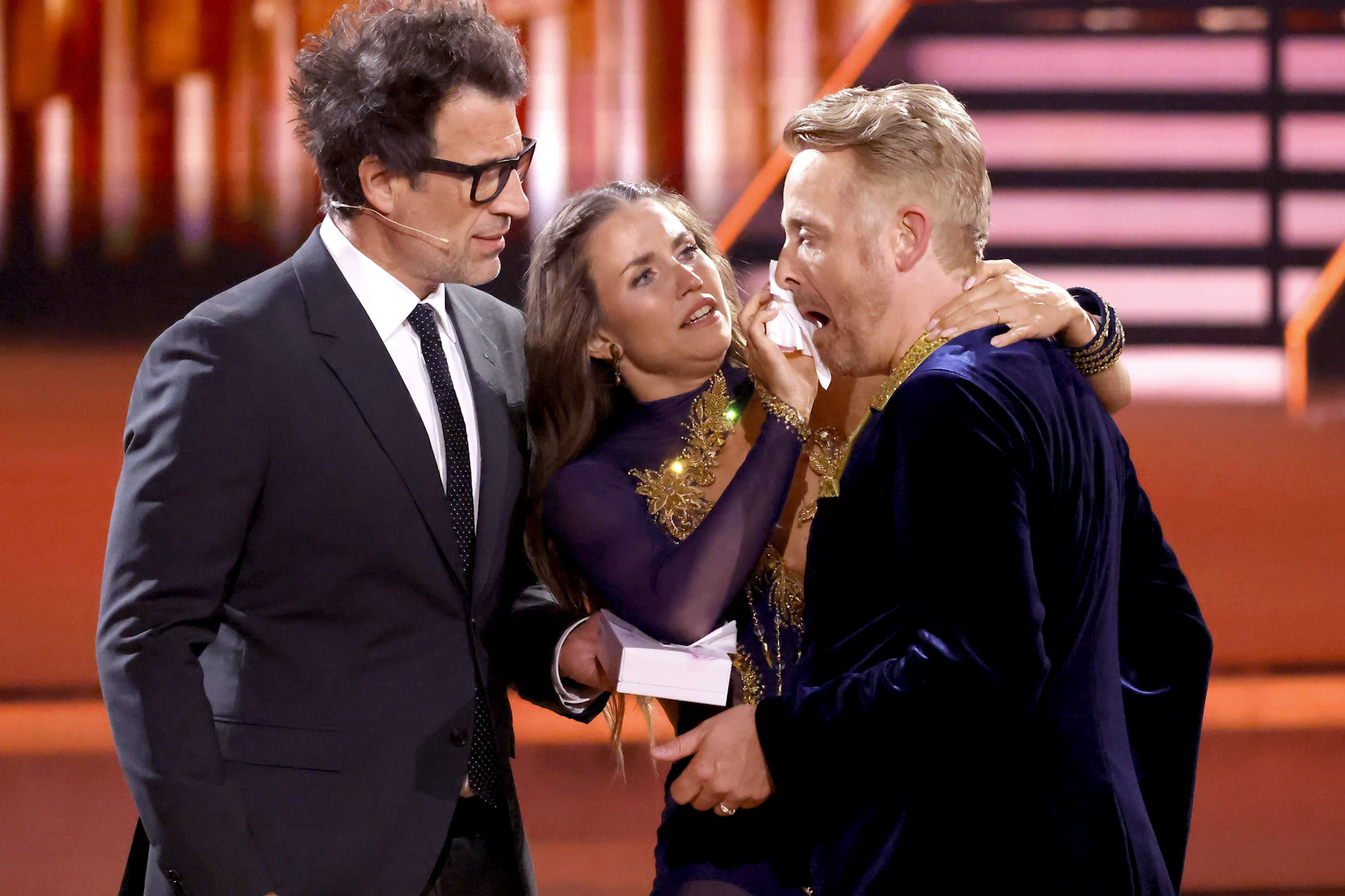 Moderator Daniel Hartwich (l.) und Profitänzerin Mariia Maksina kümmern sich um die blutende Wunde von Ross Antony. 