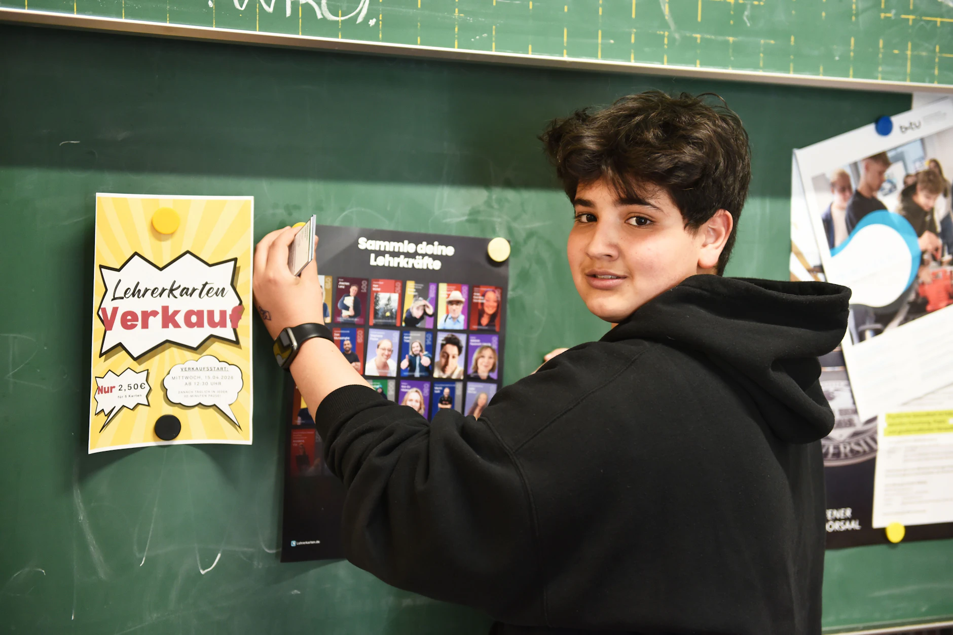Robin bringt ein Werbeplakat für den Lehrerkarten-Verkauf an. In den Pausen stehen die Schüler Schlange.