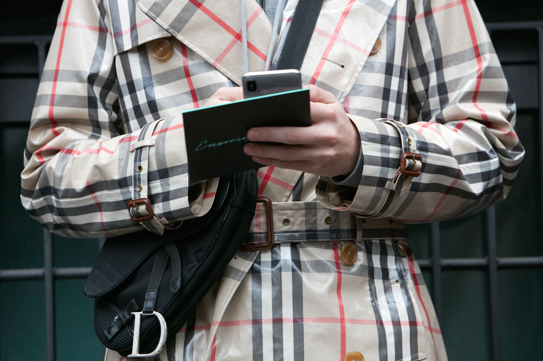 Streetstyle auf der Mailänder Modewoche: Ein Mann im Burberry-Regenmantel und mit schwarzer Dior-Tasche checkt sein Smartphone.