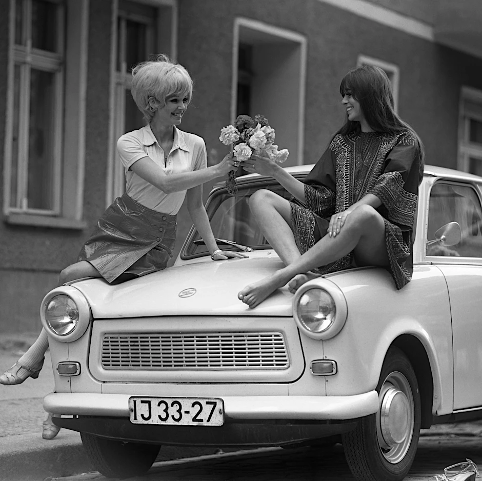 In der DDR gab es noch ein anderes Leben jenseits der SED-Diktatur: Zwei Frauen mit einem Blumenstrauß posieren auf einem Trabi für einen Modefotografen – ein Bild aus den 70er Jahren, das für viele Ostdeutsche auch ein Stück Heimat vermittelt.