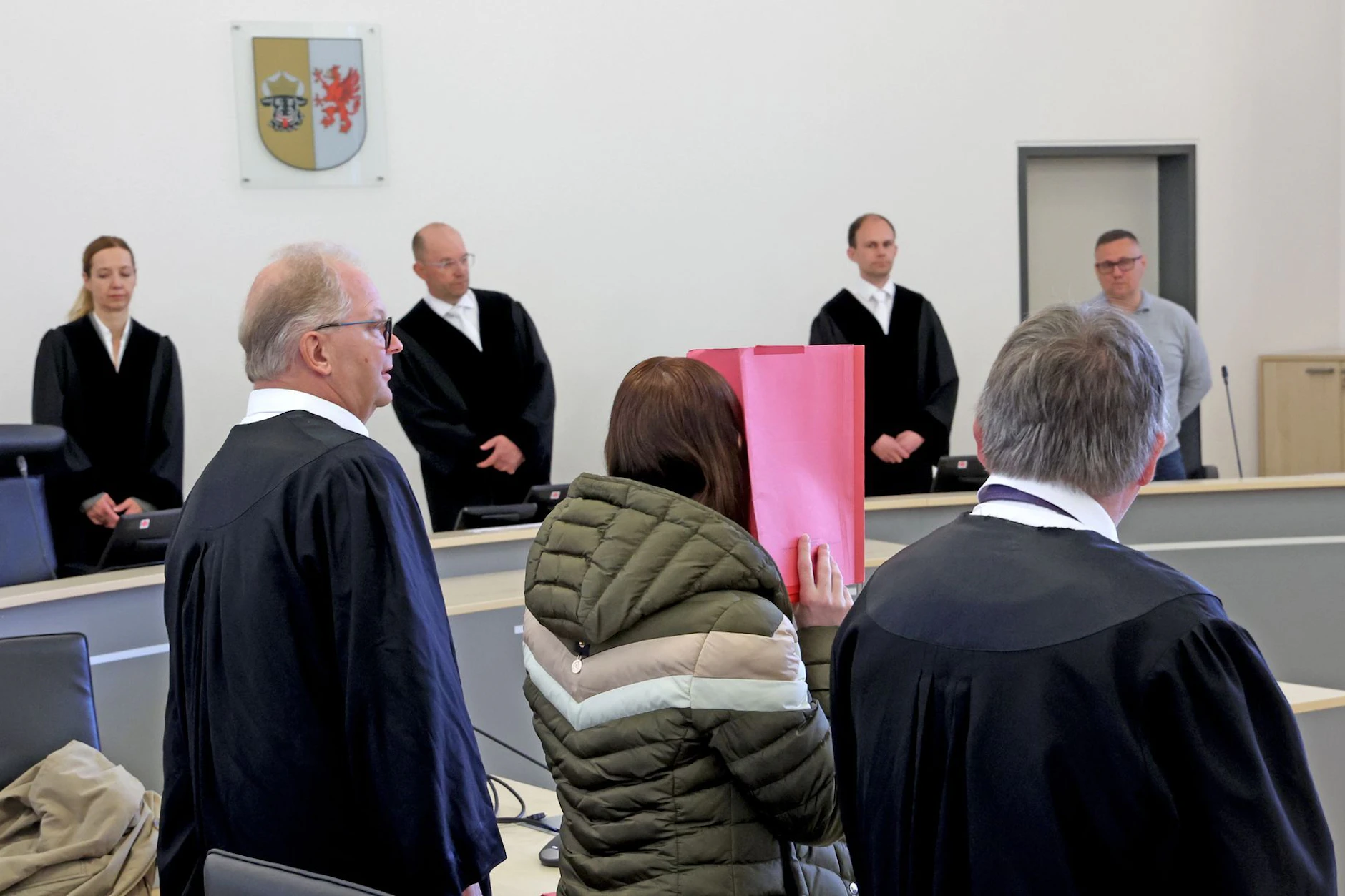 Die Angeklagte Gina H. im Prozess um Fabian aus Güstrow: Sie versteckt sich hinter einem roten Hefter, links und rechts stehen ihre Anwälte.