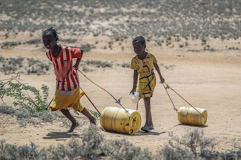 Kinder ziehen Wasserkanister durch eine trockene Landschaft in Ostafrika.