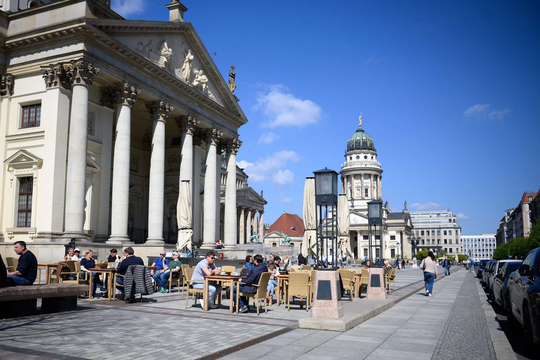Gäste sitzen bei strahlendem Sonnenschein in einem Café am Berliner Gendarmenmarkt.