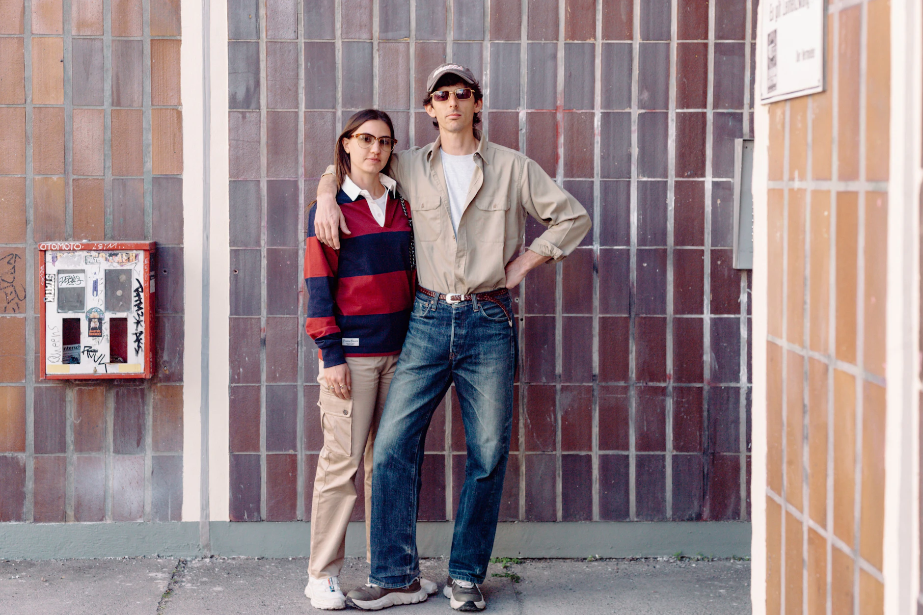 Eine Geburtstagseinladung zieht das Paar aus Italien in die Hauptstadt. Aber erst mal statten sie ein paar Galerien einen Besuch ab. Dafür hat Andrea eine japanische Vintage-Jeans von Sugar Cane anzogen, dazu ein US-Workwear-Shirt. Auf seiner Kappe steht „Boteca“, die Marke eines Kumpels aus Mailand. Ylenia hat zum gestreiften Shirt von Rowing Blazers eine Cargo-Hose von Miu Miu kombiniert. Von ebendiesem italienischen Luxuslabel stammt auch ihre dezent getönte Sonnenbrille.