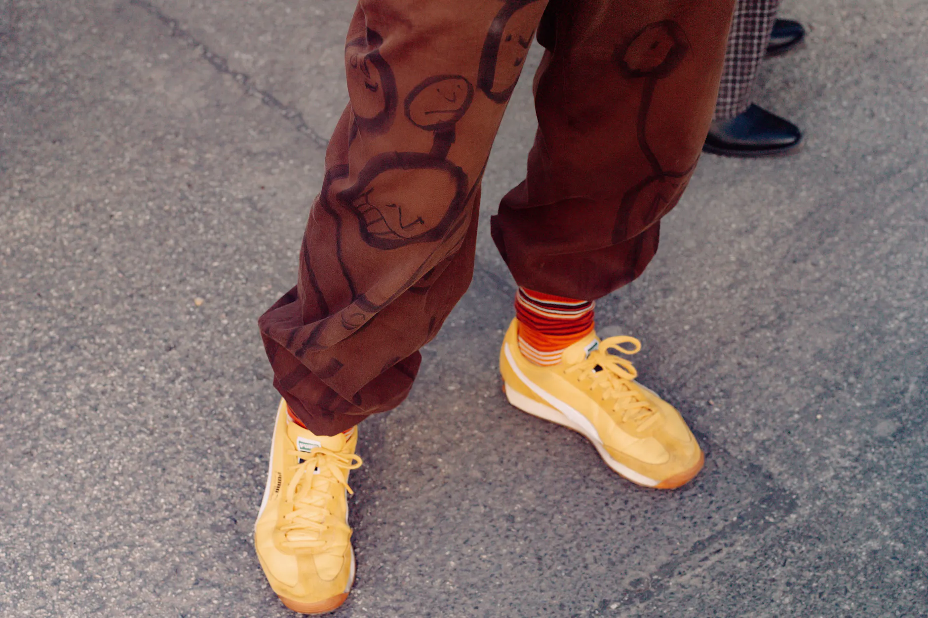 Die gestreiften Socken bilden den perfekten Übergang von der rostbraunen, mit Marken bemalten Hose zu den gelben Puma-Sneakern.