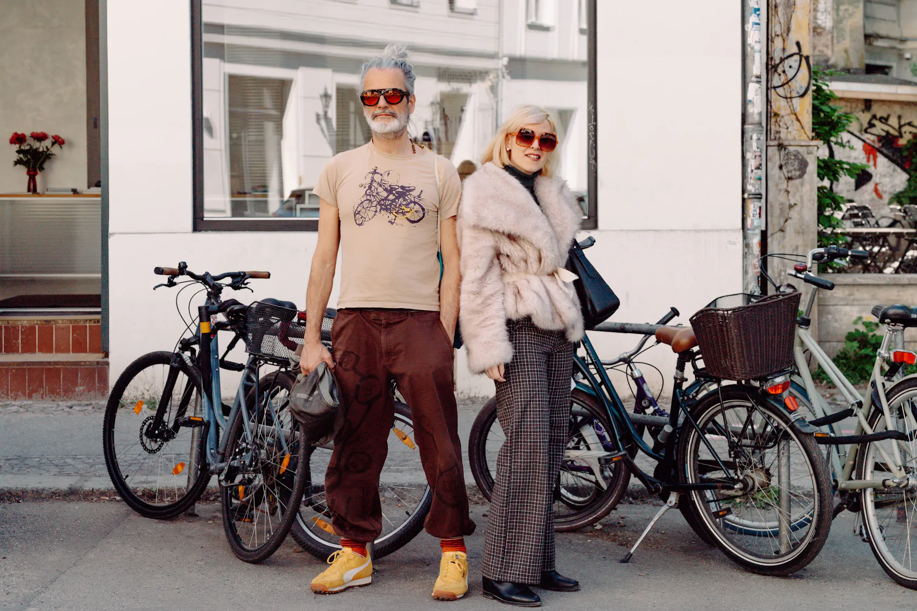 „Hose, Sneaker und ein T-Shirt “, so fasst Illustrator Michele sein Outfit pragmatisch zusammen – faktisch einwandfrei, doch eine kleine Untertreibung. Die Kleidung habe er vor zehn Jahren irgendwo in Italien gekauft, die gelben Stickereien und die Illustrationen auf der Hose stammen von ihm selbst, echte Unikate mit persönlicher Note. Aus Italien zu Besuch in der Hauptstadt: Micheles Freundin Laura, die von Kopf bis Fuß in Secondhand gekleidet ist. Mit den hohen Temperaturen habe sie nicht gerechnet, dafür gibt die voluminöse Fake-Fur-Jacke dem Look aber das nötige Drama. Michele habe ihr davon abgeraten, in Berlin mit Echtpelz herumzulaufen.