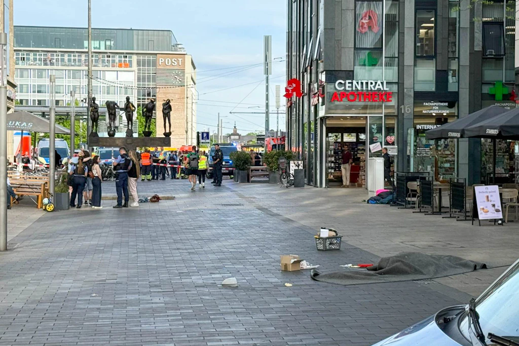 Die Polizei sperrt den Bereich weiträumig ab, auf der Straße ist mutmaßlich eine abgedeckte Person zu erkennen. 