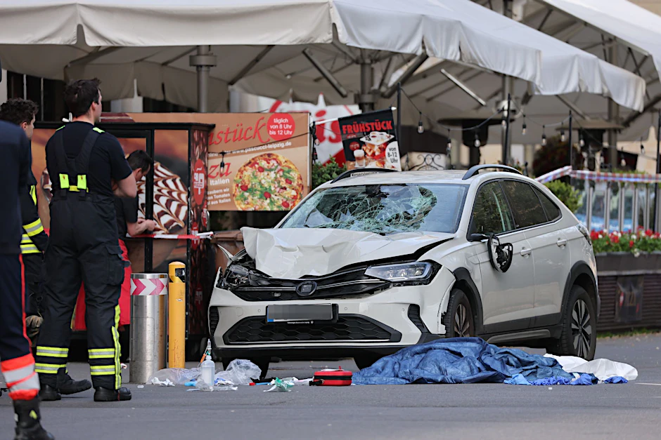 Rettungskräfte stehen am beschädigten VW an der Stelle, wo das Auto in eine Menschengruppe gefahren ist. 