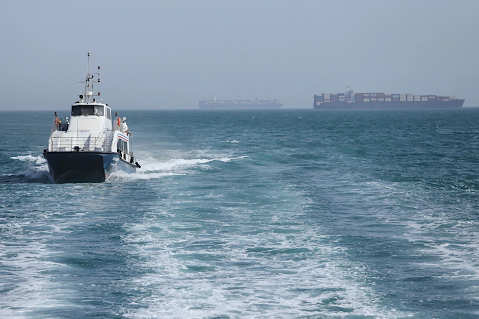Ein Patrouillenboot fährt durch das Wasser, während Frachtschiffe in der Straße von Hormus vor Bandar Abbas, Iran, vor Anker liegen.