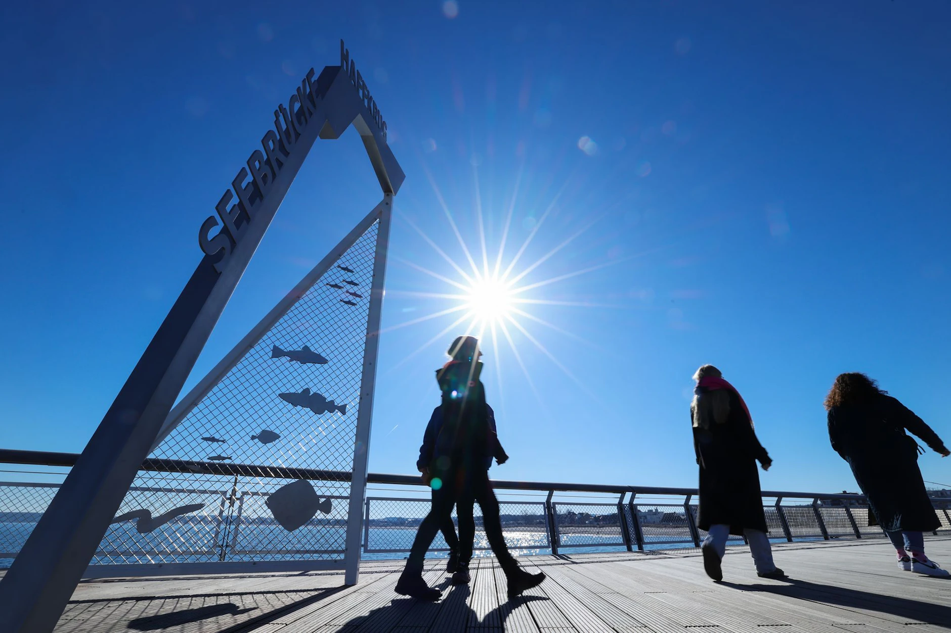 Spaziergänger sind bei strahlendem Sonnenschein auf der Seebrücke Haffkrug am Ostseestrand unterwegs. 