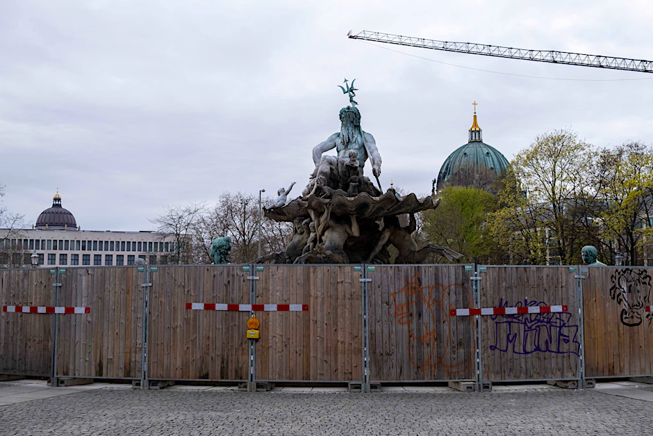 Der Berliner Neptunbrunnen hinter einem Bauzaun im April