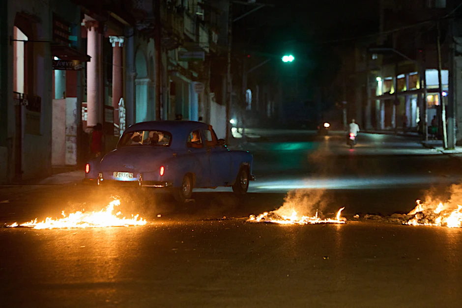 Menschen fahren mit einem amerikanischen Oldtimer durch eine Barrikade in Havanna, die von Anwohnern errichtet wurde, die gegen anhaltende Stromausfälle zu protestieren.