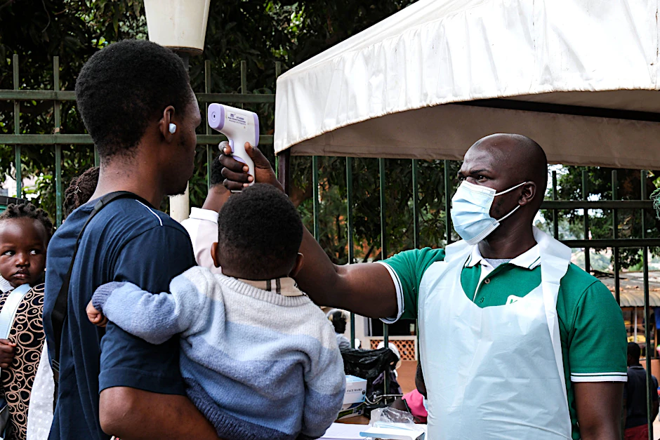 Ein Gesundheitsbeamter untersucht Menschen mit einem Thermometer vor einem Krankenhaus in Kampala.