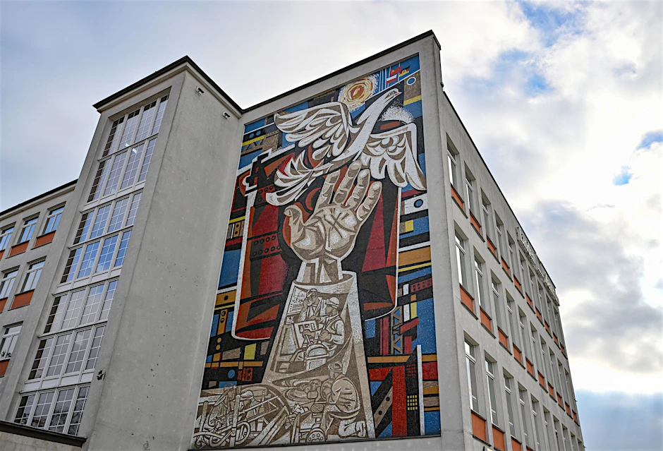 An einer Fassade eines ehemaligen Kaufhauses in Eisenhüttenstadt ist ein großes Mosaik-Kunstwerk von Walter Womacka (1925 - 2010) zu sehen. Die Stadt lädt erneut zum Probewohnen ein - mit einem konkreten Ziel.