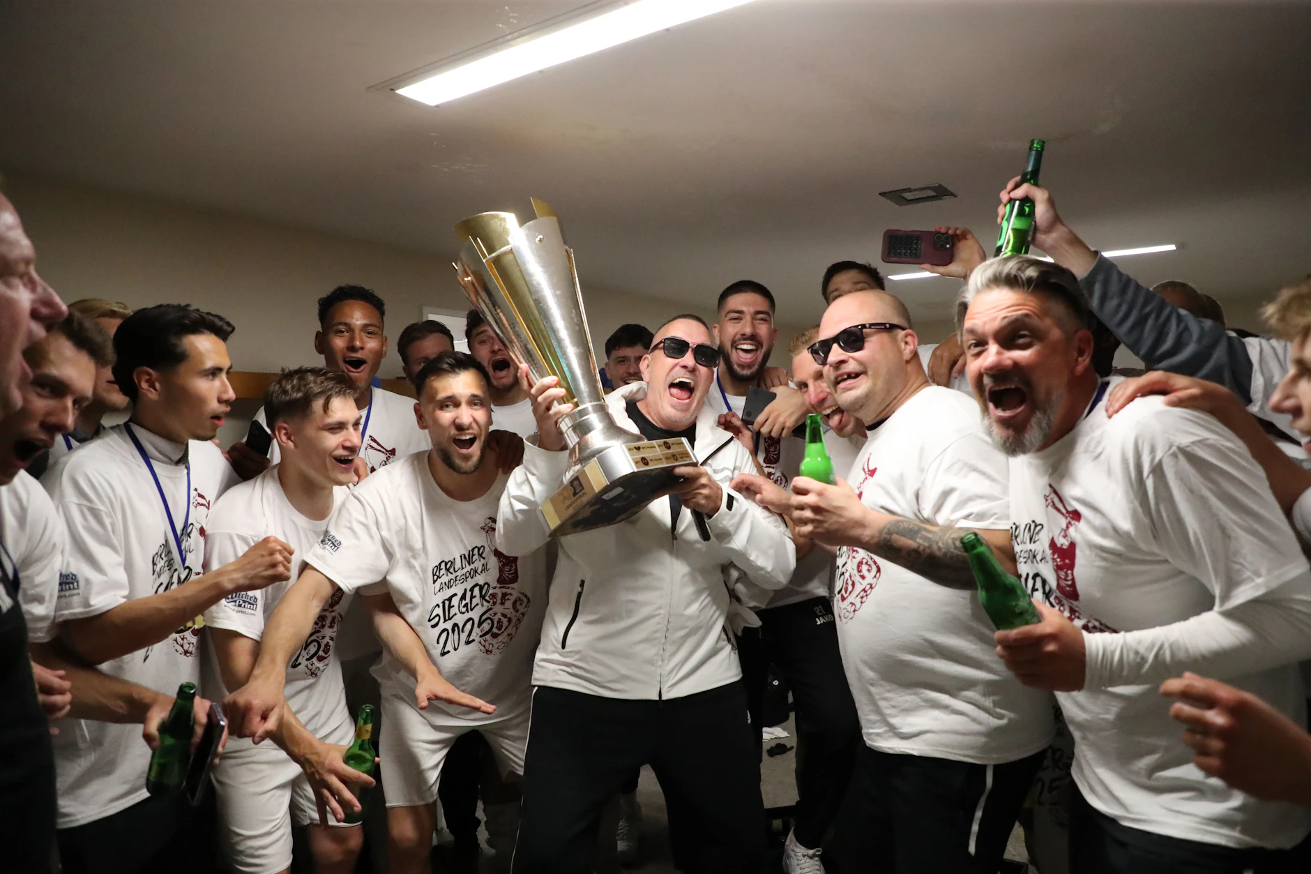 Ausgelassener Partymoment: Peter Meyer (M.), Wirtschaftsratsvorsitzender des BFC Dynamo, feiert in der Kabine mit der Mannschaft den Pokalsieg 2025.