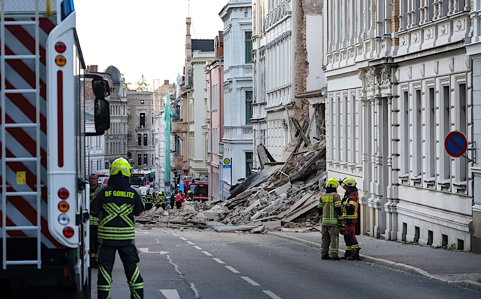 Einsatzkräfte von Polizei und Feuerweht stehen in der Nähe eines eingestürzten Hauses.