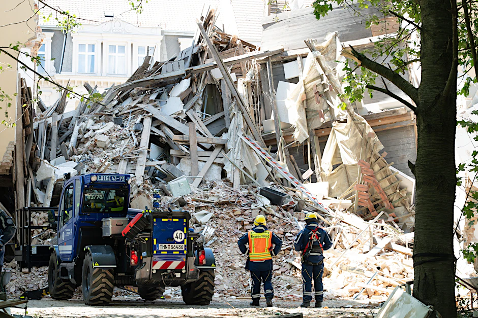 Einsatzkräfte stehen vor dem Schuttberg des eingestürzten Wohnhauses in der Innenstadt.
