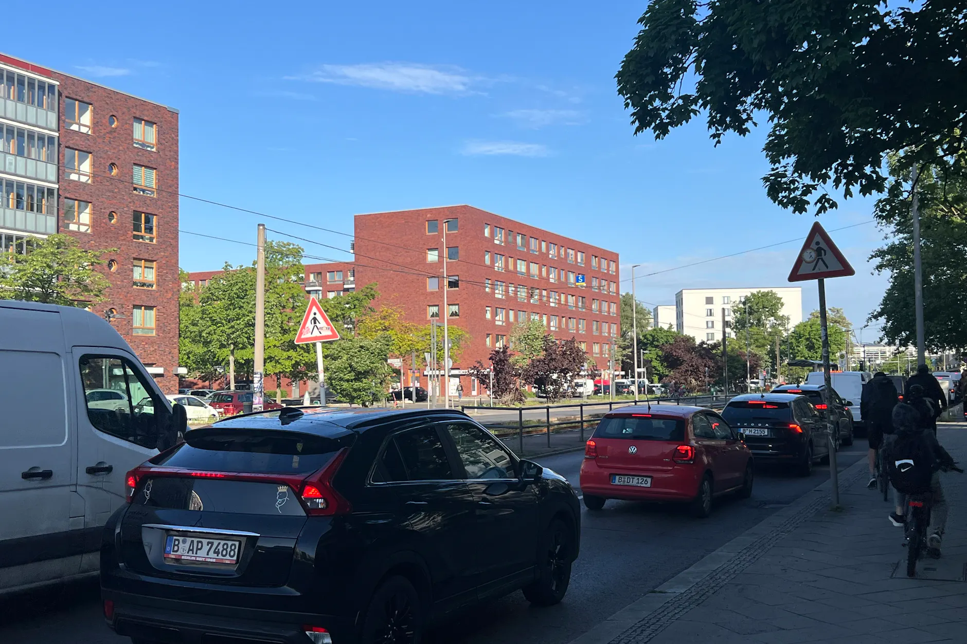 Wieder einmal dichter Verkehr auf der Hauptstraße. Die beiden Verkehrsschilder zum Fußgängerüberweg weisen auf die Gefahr hin, oft ohne Erfolg. Auch auf der Fahrbahn wird auf den Fußgängerüberweg hingewiesen. Bei Stau gehen diese aber unter.