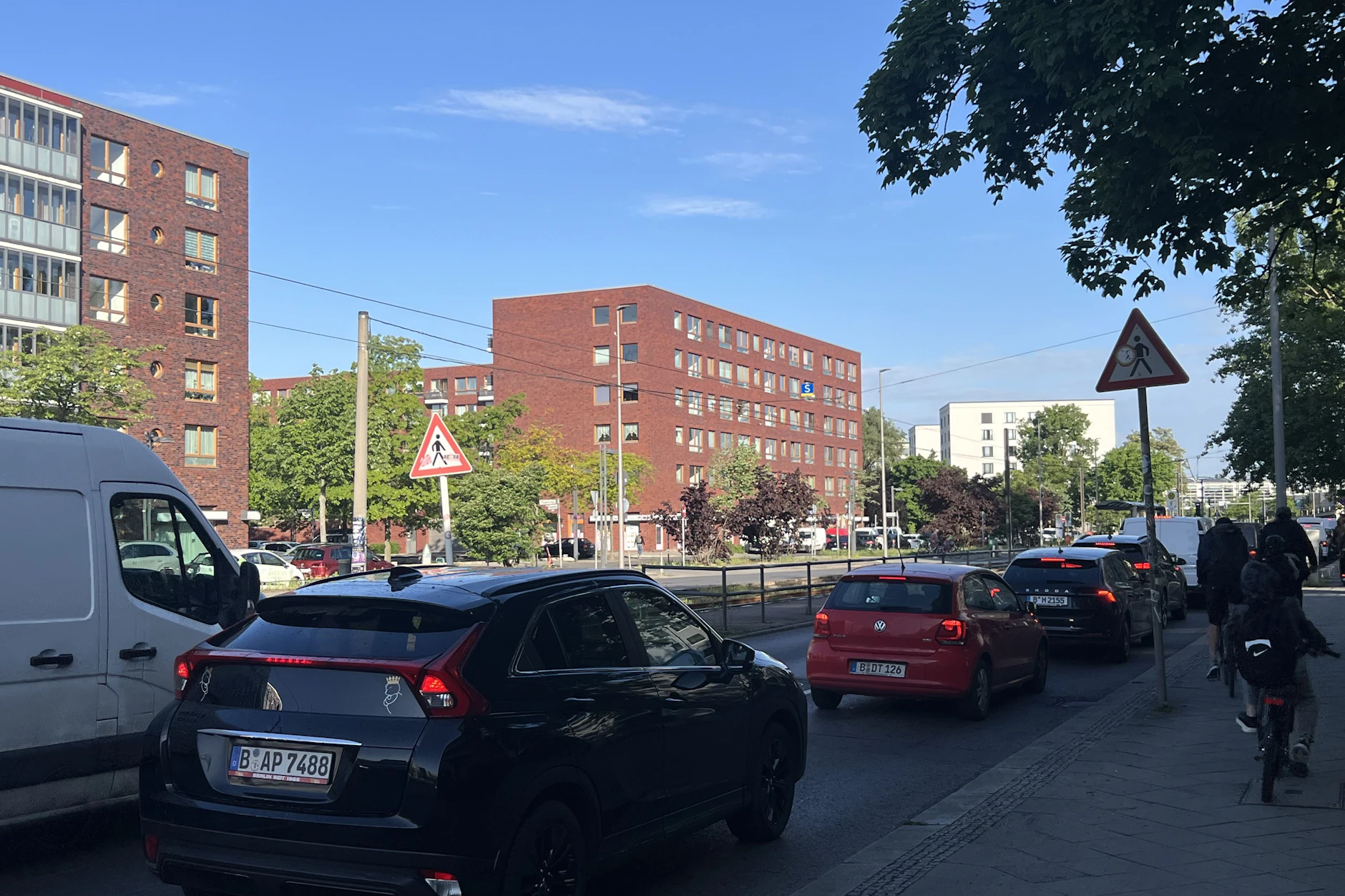 Wieder einmal dichter Verkehr auf der Hauptstraße. Die beiden Verkehrsschilder zum Fußgängerüberweg weisen auf die Gefahr hin, oft ohne Erfolg. Auch auf der Fahrbahn wird auf den Fußgängerüberweg hingewiesen. Bei Stau gehen diese aber unter.