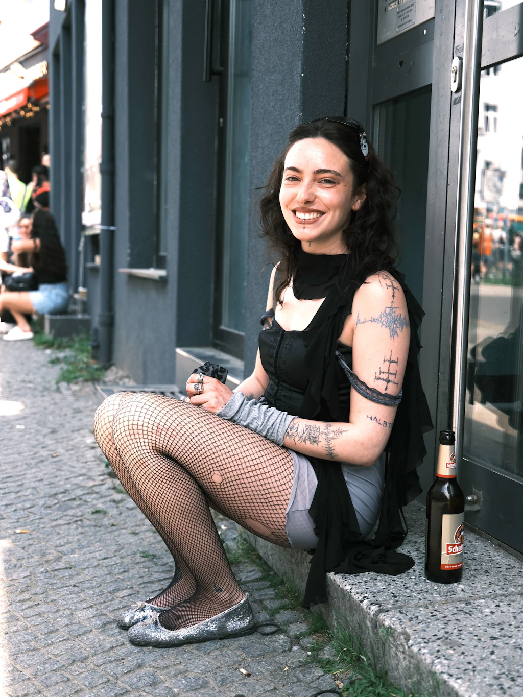 Als wir Goya fragen, ob sie bei unserer Streetstyle-Strecke mitmachen möchte, ist sie anfangs zwar noch nicht so richtig überzeugt – umso mehr freuen wir uns, dass sie schlussendlich doch zugestimmt hat. Sie kauft ausschließlich Second-Hand. Ihr heutiges Outfit aus einem schwarzen Korsett-Top, einer Netzstrumpfhose und silber glitzernden Ballerinas spiegelt dabei allerdings nicht ihren typischen Alltagsstil wider, sondern ist einfach das, wonach sie sich „heute am Morgen gefühlt“ hat. Nach dem Karneval der Kulturen geht es für sie noch weiter, um eine Freundin auf dem Flohmarkt zu besuchen – und wer weiß, vielleicht warten dort ja schon die nächsten Second-Hand-Schätze.
