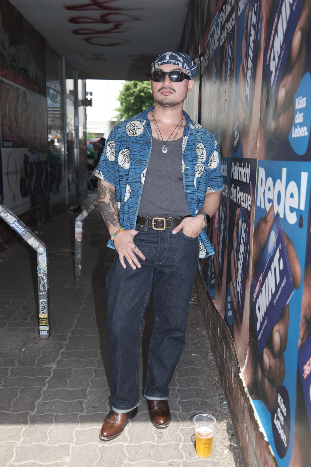 Victor ist vor einem Jahr von den Philippinen nach Berlin gezogen, heute feiert er seinen allerersten Karneval der Kulturen. Die Inspiration für seinen Look: „Japanese Amekaji“ – die japanische Adaption von Vintage-Americana. Die meisten Teile hat er auch direkt in Japan erworben. Er kombiniert eine dunkle Raw-Denim-Jeans und braune Lederboots mit einem grauen Tanktop und einem locker sitzenden, blau gemusterten Kurzarmhemd. Das passende blaue Bandana auf dem Kopf und die Sonnenbrille runden den coolen Vintage-Look perfekt ab.
