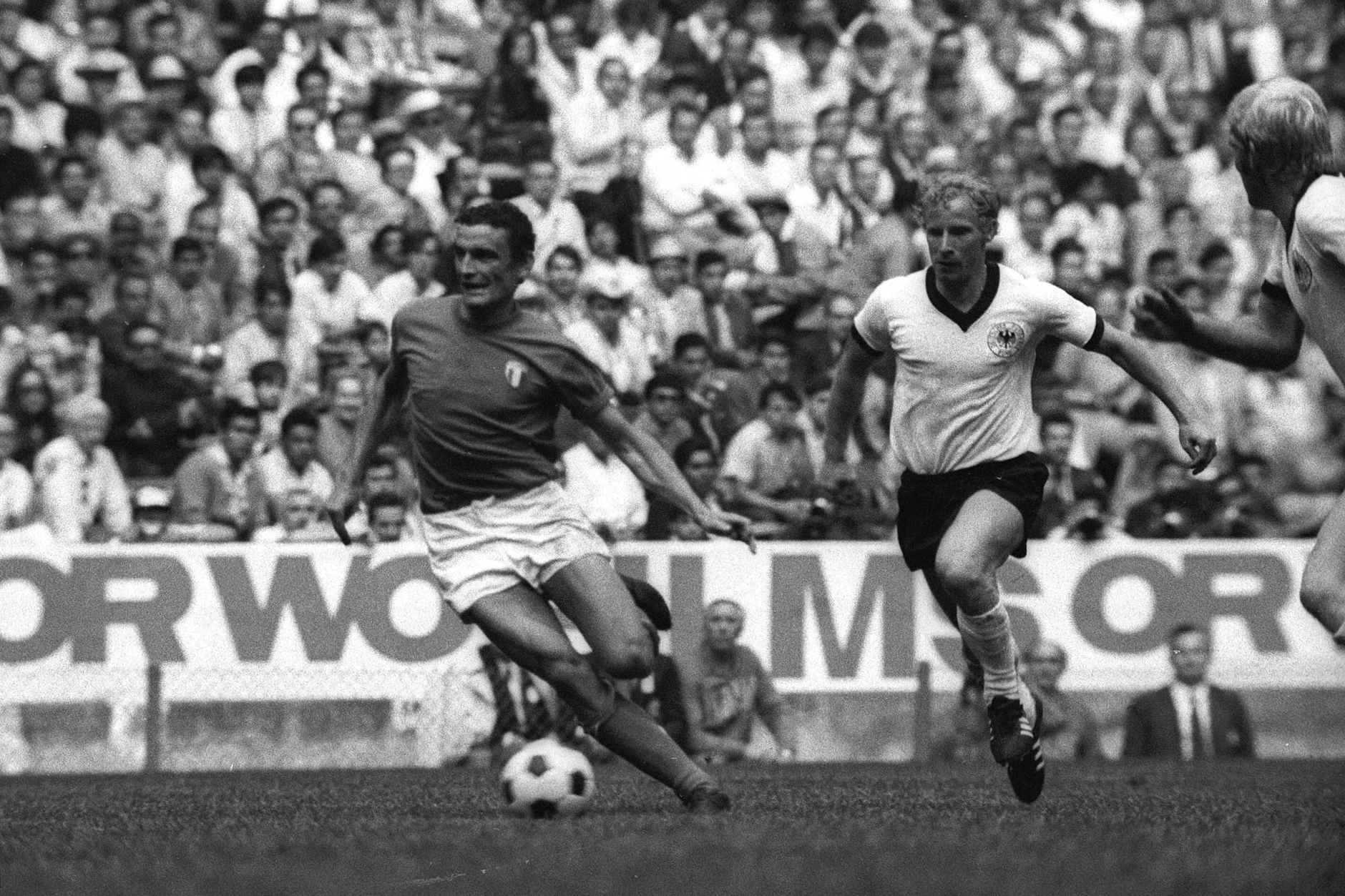 WM 1970 in Mexiko: Das Jahrhundertspiel zwischen Deutschland und Italien im Halbfinale. Berti Vogts im Laufduell mit Luigi Riva. Im Hintergrund Bandenwerbung für das DDR-Produkt ORWO.