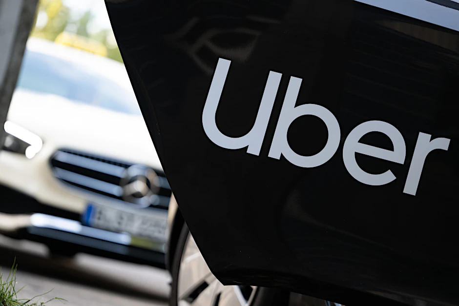 Ein Mietwagen mit einem Schriftzug des Mobilitätsdienstleisters und Fahrtenvermittlers Uber steht vor einem Taxi.