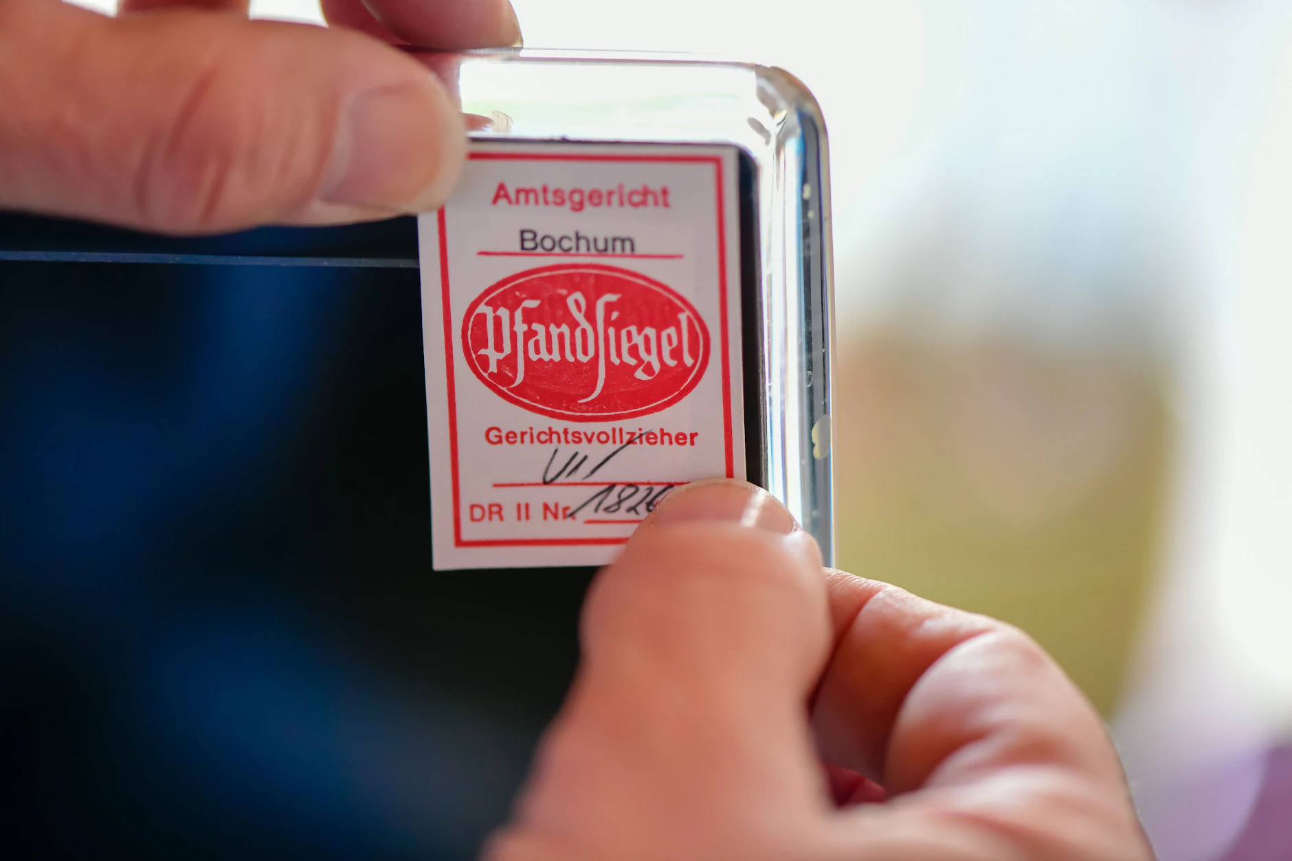 Ein Gerichtsvollzieher klebt ein Pfandsiegel auf einen Computerbildschirm.