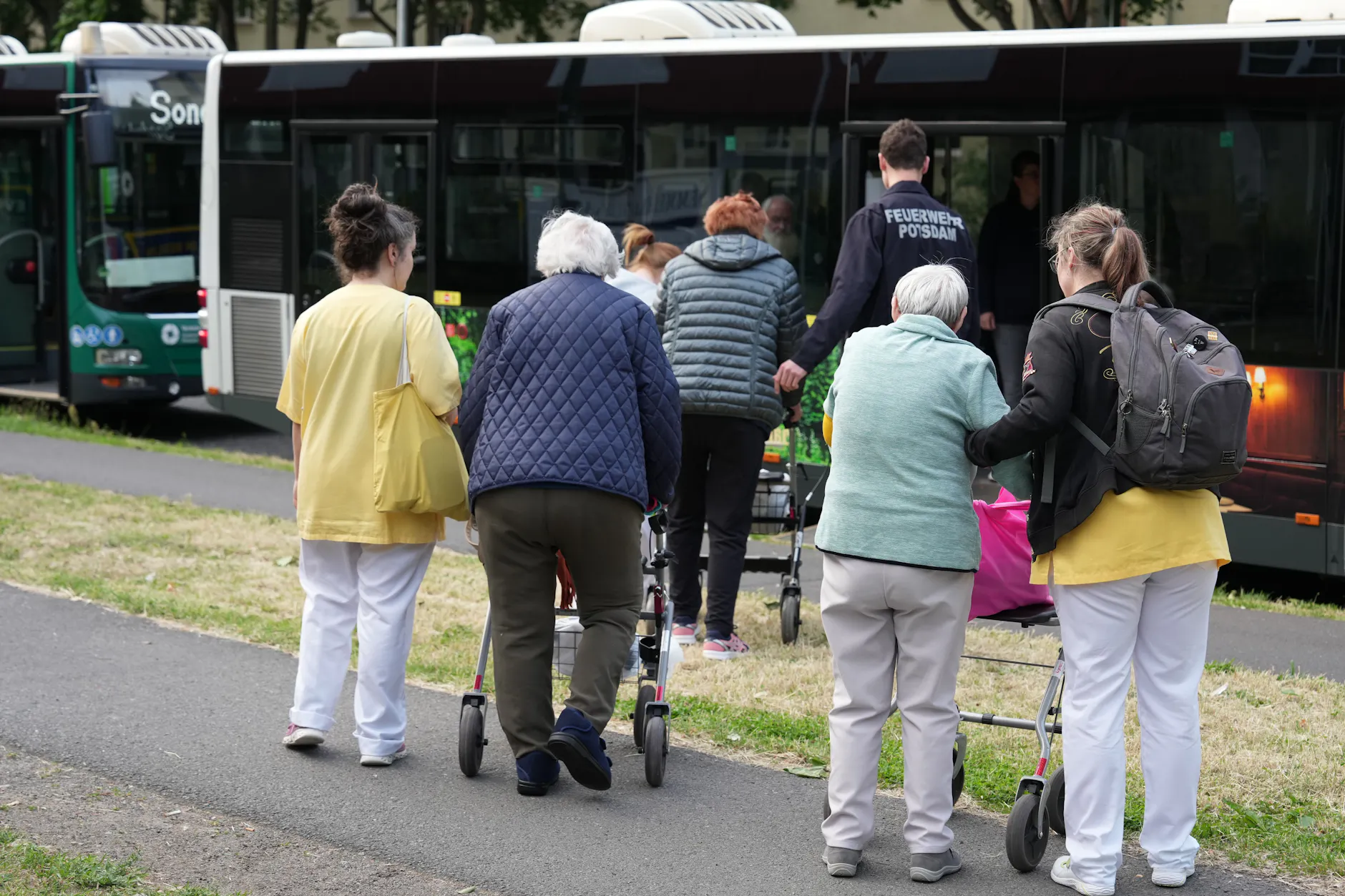 Pflegepersonal begleitet Heimbewohner mit Rollatoren zum Evakuierungsbus – ein Mitglied der Feuerwehr Potsdam hilft beim Einsteigen.