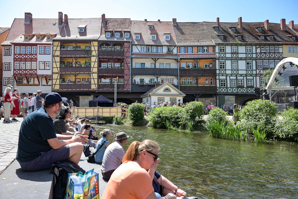 Zahlreiche Besucher sitzen am Ufer der Gera und blicken zur historischen Krämerbrücke.