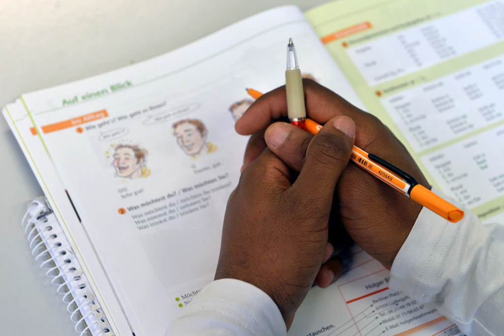 Ein Lehrbuch liegt in einem Deutschkurs für Flüchtlinge vor einem jungen Mann auf dem Tisch.