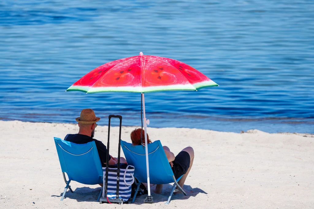 Urlauber sitzen bei hochsommerlichem Wetter unter einem Sonnenschirm am Ostseestrand. 