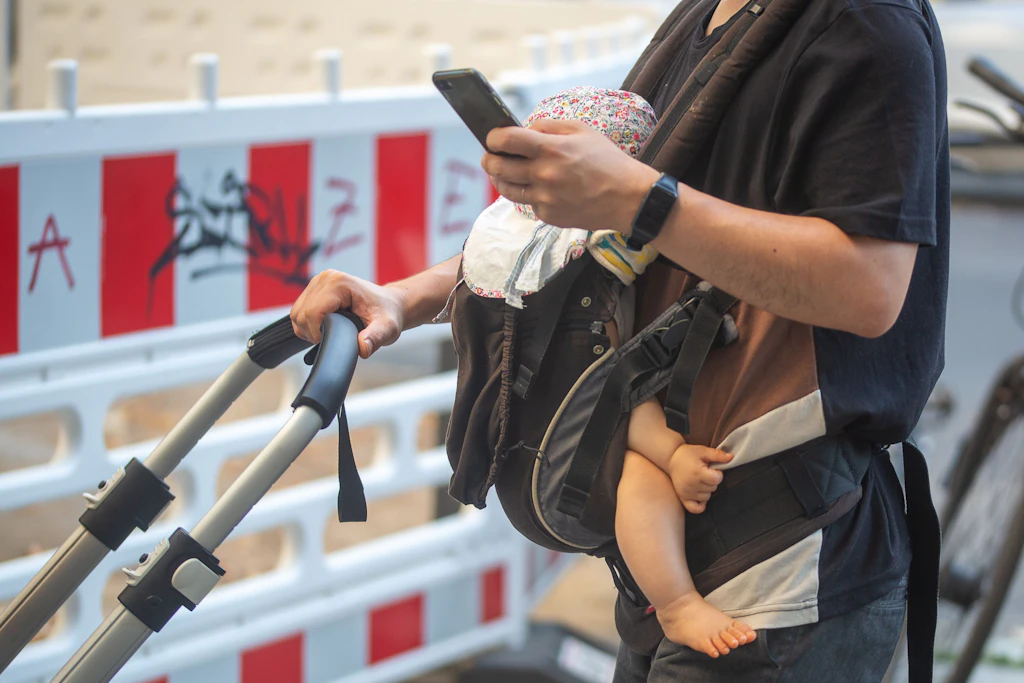 Ein Mann schiebt einen Kinderwagen und trägt gleichzeitig ein Baby in einer Tragehilfe.